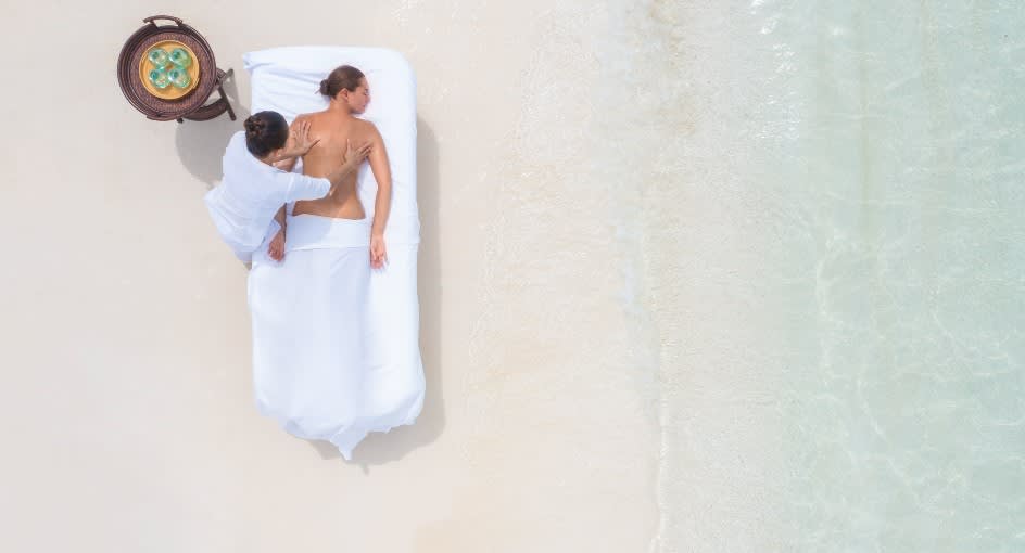 Guest enjoying a relaxing private wellness massage on the beach at Naladhu Private Island Maldives