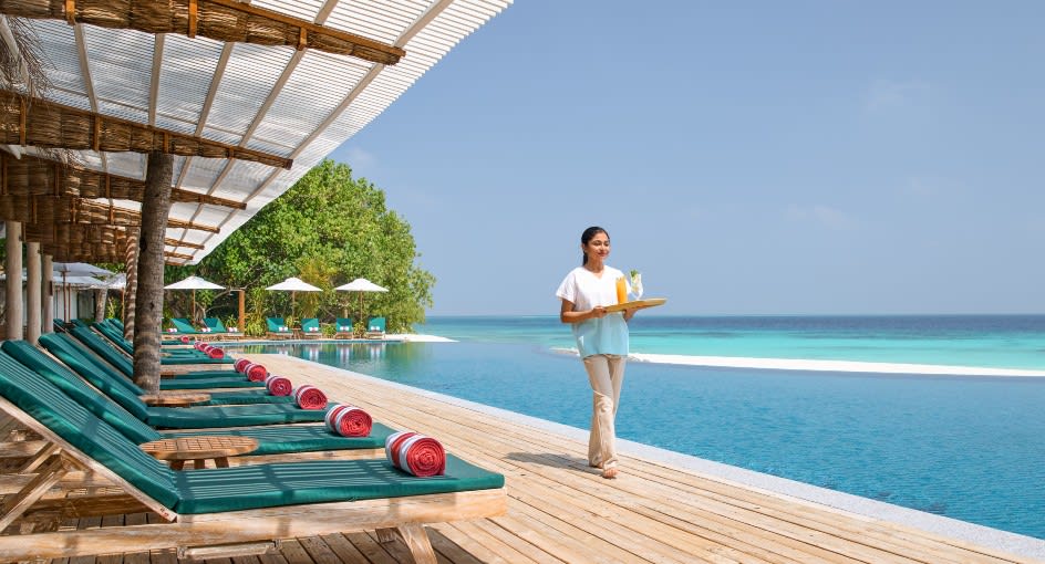 Poolside deck with sun loungers and infinity pool overlooking the ocean at NH Collection Maldives Reethi Resort