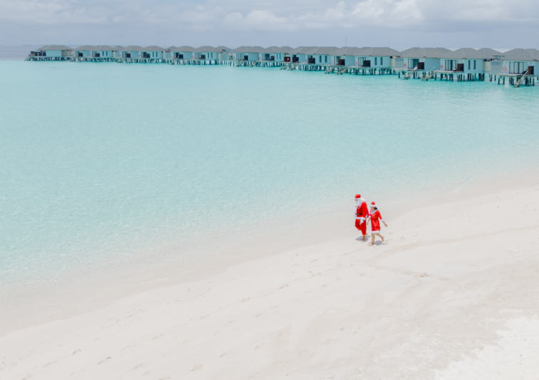 Santa and Mrs Claus walking barefoot on the beach in front of overwater villas during the festive season at NH Collection Maldives Havodda