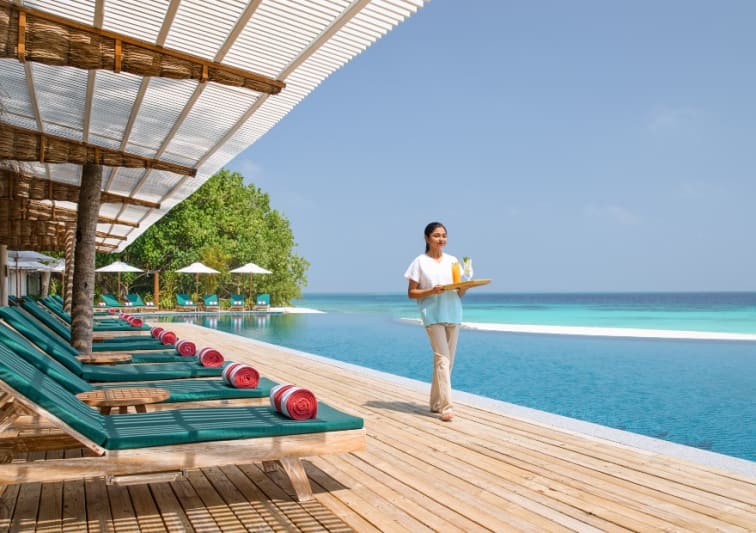 Poolside deck with sun loungers and infinity pool overlooking the ocean at NH Collection Maldives Reethi Resort