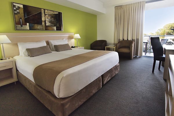 Hotels in Townsville with king size bed in hotel room bedroom with desk for work and balcony with views of Townsville at Oaks Gateway Suites